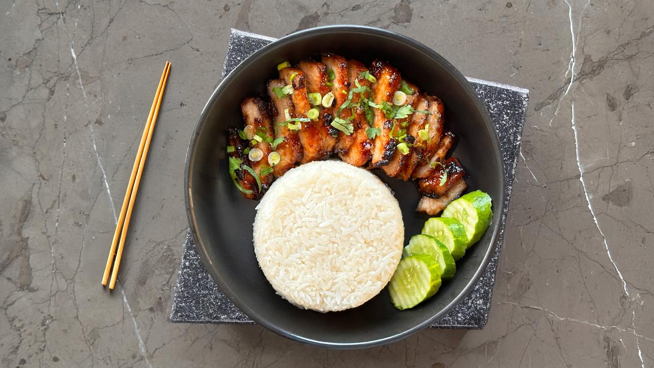 BBQ pork slices, jasmine rice and cucumber in a black bowl