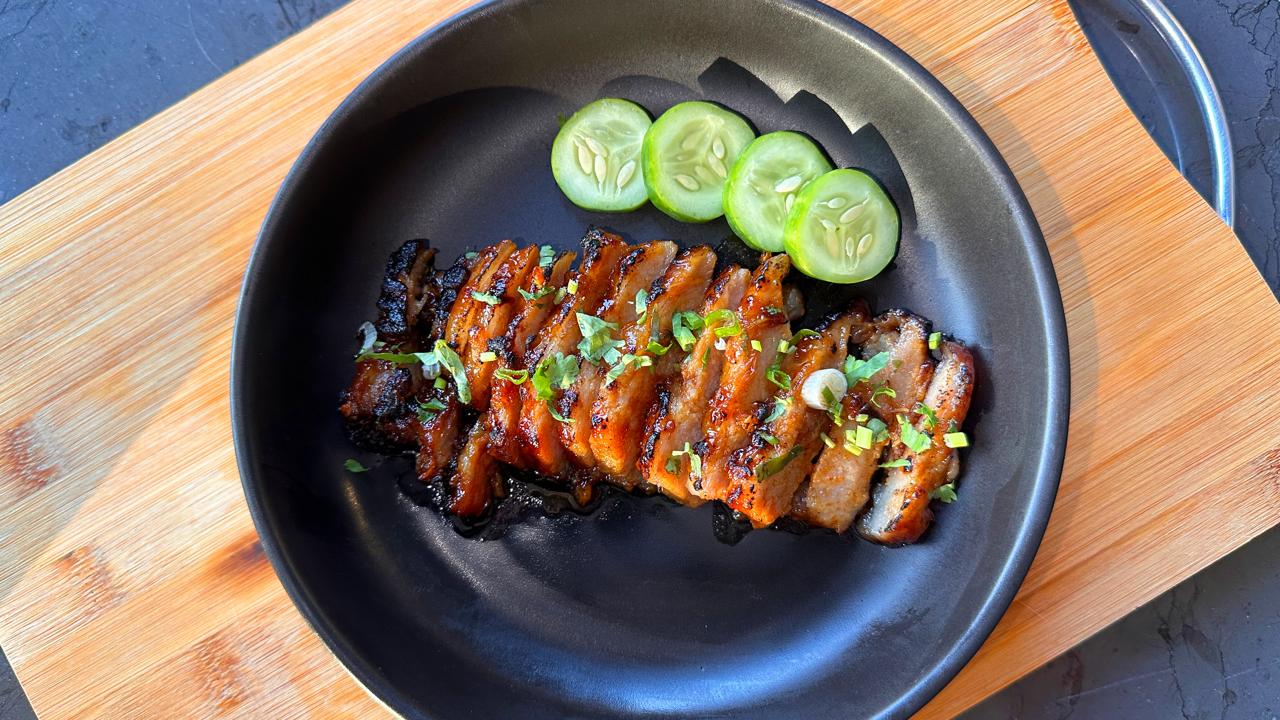 Sliced grilled pork and cucumber on a black plate