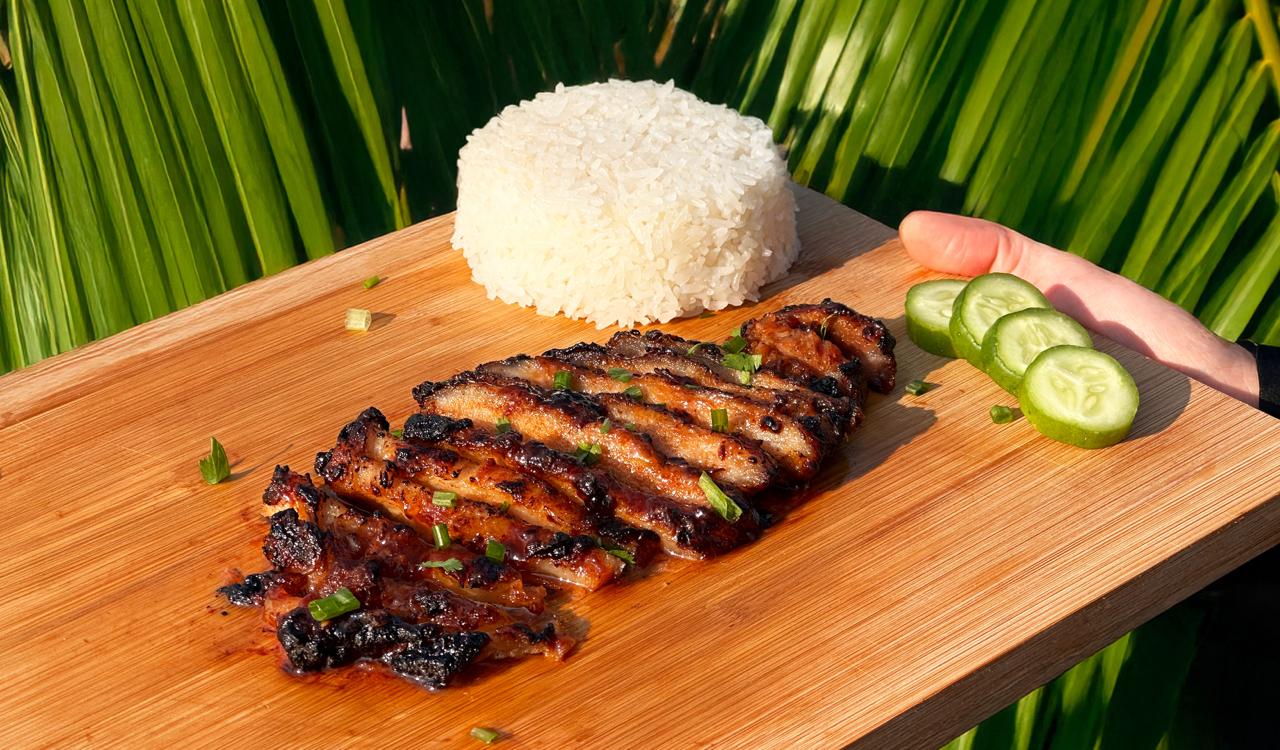 BBQ pork, rice and cucumber arranged on a wooden board